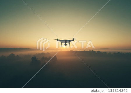 A drone soars above a foggy valley as the sun rises, illuminating the horizon with warm colors in the early morning sky 133814842