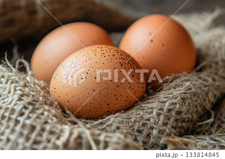 Three brown eggs with speckles are placed on textured burlap fabric, creating a warm and natural kitchen atmosphere Three brown eggs with speckles are placed on textured burlap fabric, creating a warm and natural kitchen atmosphere 133814845