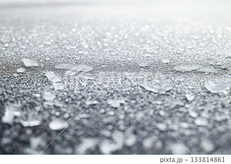 Morning frost creates a shimmering layer of ice shards on a dark surface, reflecting the soft light of dawn 133814861