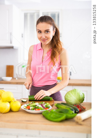 Positive woman is cutting vegetables for salad in kitchen at home 133815258