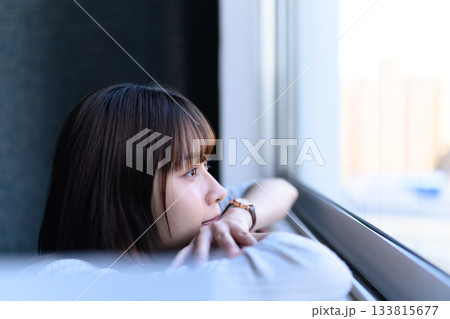 窓の外を見つめる若い女性の横顔、物思いにふける様子 窓の外を見つめる若い女性の横顔、物思いにふける様子 133815677