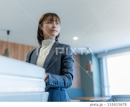 オフィスで書類を持ち、遠くを見つめる若い日本人女性ビジネスパーソン 133815678