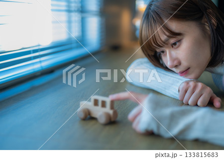 窓辺で木製のおもちゃの車を愛おしそうに見つめる若い女性 133815683