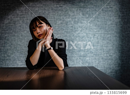 憂鬱そうな表情でテーブルに肘をつく若い女性 133815699
