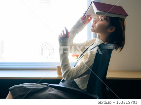 椅子に座り本を頭に乗せてリラックスする若い日本人女性 133815703