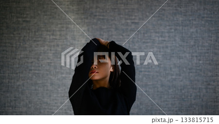 暗い背景の前で腕を上げる若い日本人女性のドラマチックな上半身ポートレート 暗い背景の前で腕を上げる若い日本人女性のドラマチックな上半身ポートレート 133815715
