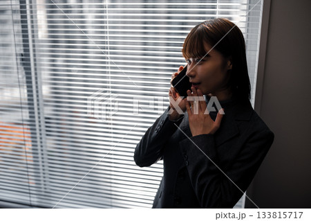 ブラインド越しの窓際で内緒話をする若いビジネスウーマン 133815717