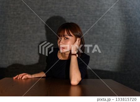 暗い部屋でテーブルに肘をつき思案する若い女性 133815720