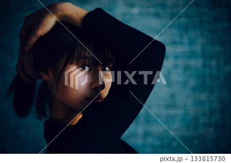 暗闇の中、片手を頭にやりポーズをとる若い女性 133815730