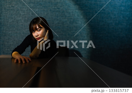 暗い部屋でテーブルに肘をつき物思いにふける若い女性 133815737