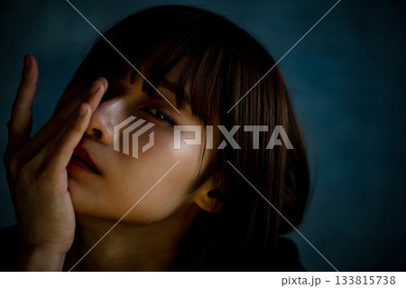 暗闇の中、顔の一部を覆う憂鬱な表情の20代女性の上半身ポートレート 暗闇の中、顔の一部を覆う憂鬱な表情の20代女性の上半身ポートレート 133815738