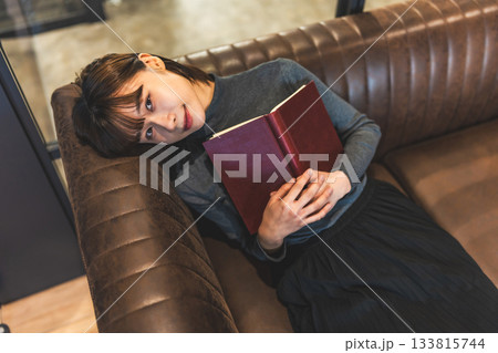 革張りのソファで本を抱きかかえて微笑む若い女性 133815744