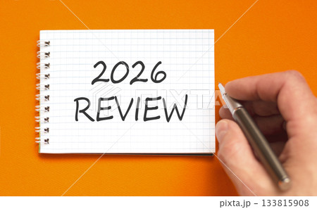 2026 Review symbol. Concept words 2026 Review on beautiful white note. Beautiful orange paper background. Businessman's hand with pen. Business and 2026 review concept. Copy space. 133815908