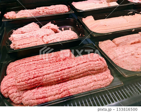 Ground Meat Patties and Sausages in Refrigerator Case. Black trays filled with fresh minced meat patties and raw sausages ready for sale in supermarket refrigerated section. BBQ and cooking concept. 133816500