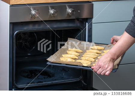 Placing Tray of Unbaked Pastries Into Open Oven in Home Kitchen Placing Tray of Unbaked Pastries Into Open Oven in Home Kitchen 133816686