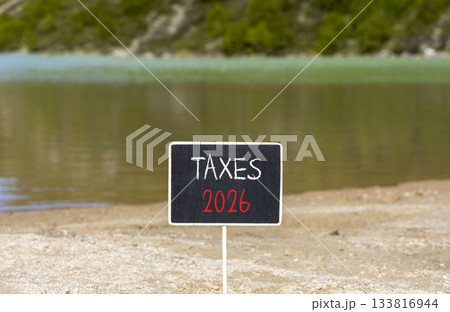 Taxes 2026 new year symbol. Concept words Taxes 2026 on beautiful black blackboard. Beautiful mountain lake sand beach background. Business and taxes 2026 new year concept. Copy space. Taxes 2026 new year symbol. Concept words Taxes 2026 on beautiful black blackboard. Beautiful mountain lake sand beach background. Business and taxes 2026 new year concept. Copy space. 133816944
