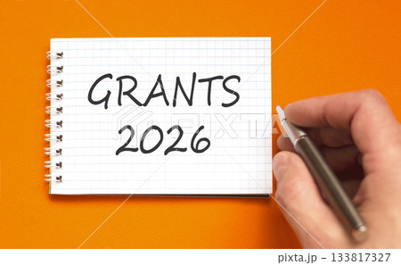 Grants 2026 symbol. Concept words Grants 2026 on beautiful white note. Beautiful orange paper background. Businessman's hand with pen. Business and grants 2026 concept. Copy space. Grants 2026 symbol. Concept words Grants 2026 on beautiful white note. Beautiful orange paper background. Businessman's hand with pen. Business and grants 2026 concept. Copy space. 133817327