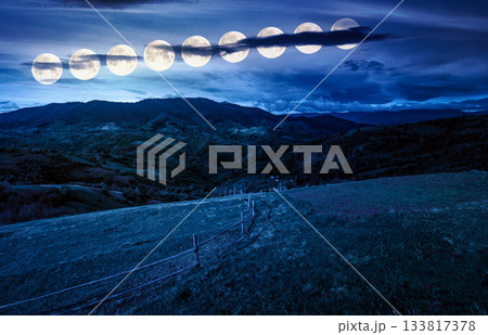 wooden fence on hillside with rural field in mountains at night. beautiful countryside landscape with rolling hills and pasture in spring in full moon light. fake news or conspiracy concepts 133817378