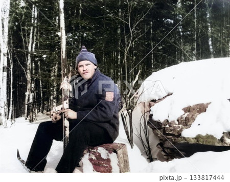 A vintage portrait of a young man sitting with cross-country skis in a snowy forest. Retro photo from 1986. 133817444