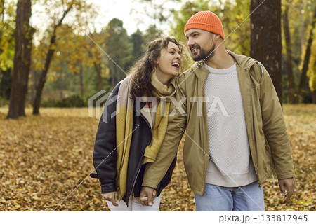 Smiling couple holding hands on a peaceful autumn stroll under colorful park trees 133817945