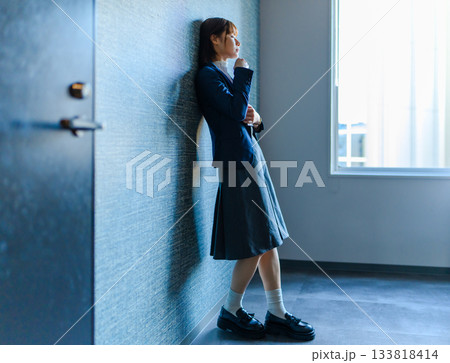 廊下で壁に寄りかかり物思いにふける女子学生 133818414
