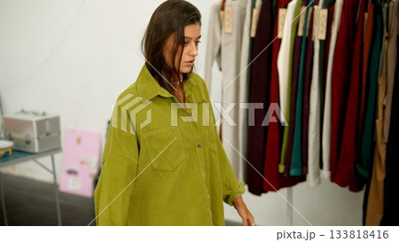 A fashion model is wearing a green oversized shirt while posing next to a clothing rack 133818416