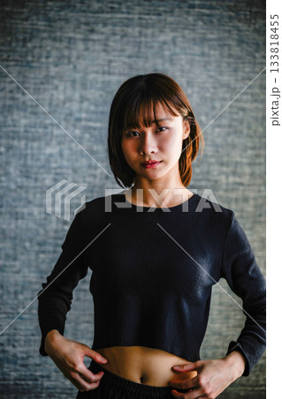 暗い背景で腹部をつまむ若い女性のポートレート 133818455