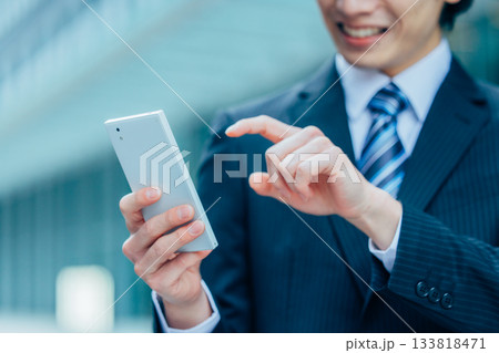 オフィスでスマホを操作する若いビジネスマンの手元 オフィスでスマホを操作する若いビジネスマンの手元 133818471