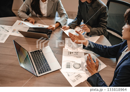 会議室で資料を広げ議論するビジネスパーソン、ノートパソコンとデータ分析 133818964