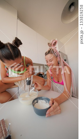Two women joyfully cooking in a bright kitchen, sharing their love for meals and laughter Two women joyfully cooking in a bright kitchen, sharing their love for meals and laughter 133819258
