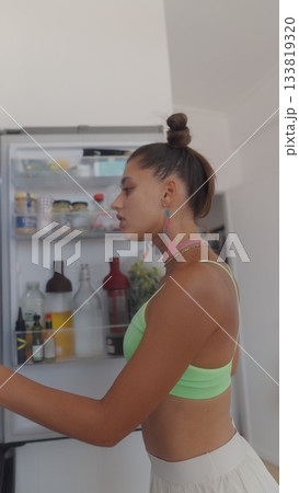 A Stylish Woman is in a Modern Kitchen Surrounded by a Bright Refrigerator and Refreshing Drinks A Stylish Woman is in a Modern Kitchen Surrounded by a Bright Refrigerator and Refreshing Drinks 133819320