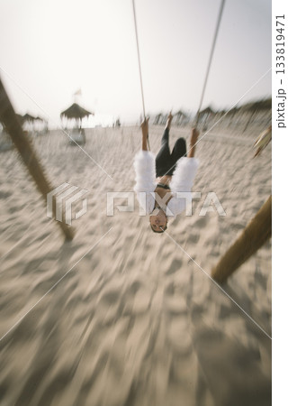 Swinging joyfully on the beautiful beach during the stunning sunset, feeling carefree and joyful 133819471