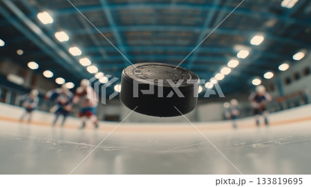 Ice hockey banner. Hockey puck resting on stadium ice with blurred athletes preparing to play Ice hockey banner. Hockey puck resting on stadium ice with blurred athletes preparing to play 133819695