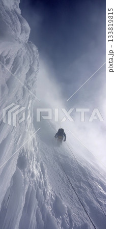 Climber trekking icy mountain ridge through dense fog. Solo mountaineer navigating a challenging snowy ridge against a foggy sky 133819815
