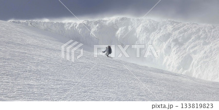 Climber trekking icy mountain ridge through dense fog. Solo mountaineer navigating a challenging snowy ridge against a foggy sky Climber trekking icy mountain ridge through dense fog. Solo mountaineer navigating a challenging snowy ridge against a foggy sky 133819823