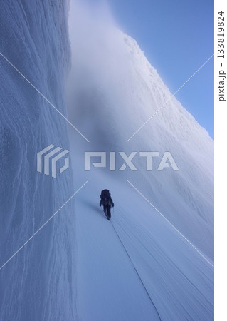 Climber trekking icy mountain ridge through dense fog. Solo mountaineer navigating a challenging snowy ridge against a foggy sky Climber trekking icy mountain ridge through dense fog. Solo mountaineer navigating a challenging snowy ridge against a foggy sky 133819824