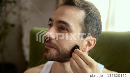 Man massaging beard line with gua sha tool in relaxed mood 133820152