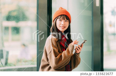 冬の街角でスマートフォンを使う笑顔の女性 冬の街角でスマートフォンを使う笑顔の女性 133821677
