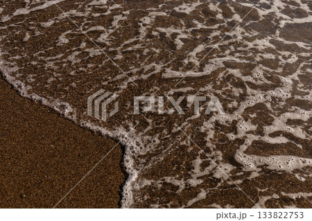 Soft waves roll in, creating foam on the shore as sunlight sparkles on the water. The sandy beach invites relaxation, with a peaceful atmosphere and warm weather Soft waves roll in, creating foam on the shore as sunlight sparkles on the water. The sandy beach invites relaxation, with a peaceful atmosphere and warm weather 133822753