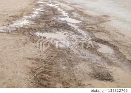 After recent rainfall, a dirt road displays puddles and wet patches surrounded by dry earth. Tire tracks mark the path, indicating vehicle passage in the countryside After recent rainfall, a dirt road displays puddles and wet patches surrounded by dry earth. Tire tracks mark the path, indicating vehicle passage in the countryside 133822763