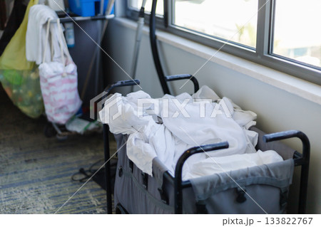 Housekeeping staff organizes clean white linens in a cart within a hotel room. The room features large windows letting in natural light, creating a neat environment Housekeeping staff organizes clean white linens in a cart within a hotel room. The room features large windows letting in natural light, creating a neat environment 133822767