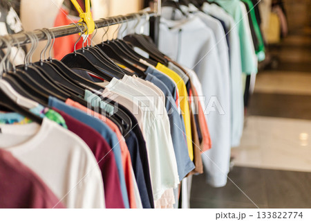 A clothing rack shows a variety of casual t-shirts and sweatshirts in different colors at a retail store. The modern setting features bright lighting and a stylish atmosphere 133822774