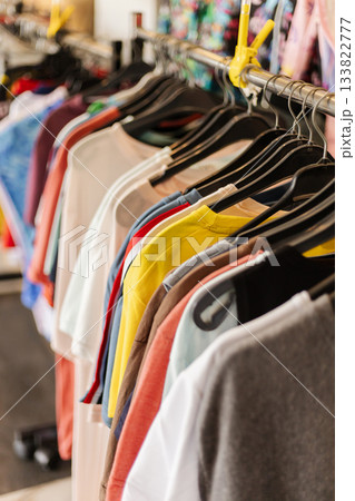 A variety of casual t-shirts in multiple colors are displayed on hangers in a bustling retail store. Shoppers explore the clothing options during daylight, creating an energetic atmosphere 133822777