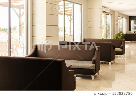 The seating area features stylish brown sofas arranged in a bright, spacious cafe. Large windows allow plenty of natural light to fill the room, creating an inviting atmosphere The seating area features stylish brown sofas arranged in a bright, spacious cafe. Large windows allow plenty of natural light to fill the room, creating an inviting atmosphere 133822780