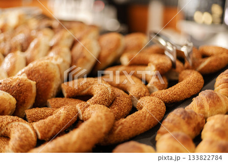 A selection of warm, golden pastries is arranged on a table in a bakery. The aroma fills the air as customers are welcomed to choose their favorites during morning hours 133822784