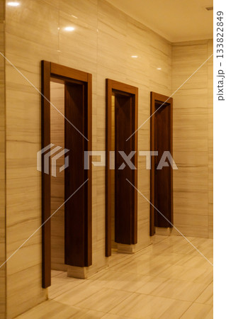 A serene hallway showcases three wooden door frames against a backdrop of smooth, light-colored marble. The warm lighting creates a calm atmosphere A serene hallway showcases three wooden door frames against a backdrop of smooth, light-colored marble. The warm lighting creates a calm atmosphere 133822849