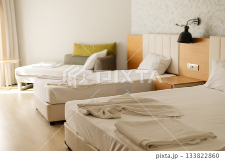 This hotel room features two twin beds with crisp white linens and simple decor. A cozy seating area with a green cushion adds style and comfort for guests This hotel room features two twin beds with crisp white linens and simple decor. A cozy seating area with a green cushion adds style and comfort for guests 133822860