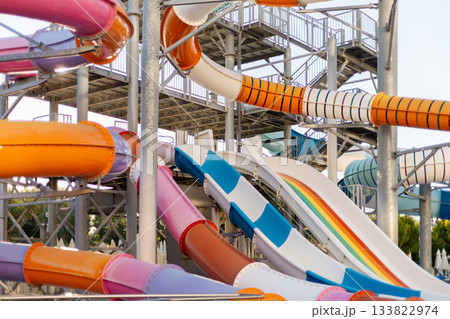 A vibrant collection of water slides in various colors stands tall at a lively water park, inviting visitors on a warm summer day. Children and families are seen enjoying the fun 133822974