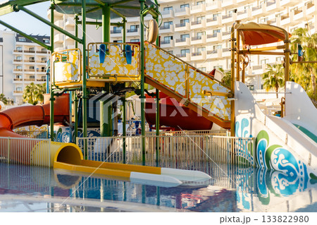 Bright water slides and play structures are found at a resort pool area, inviting families to enjoy fun activities under the sun. The vibrant colors enhance the joyful environment Bright water slides and play structures are found at a resort pool area, inviting families to enjoy fun activities under the sun. The vibrant colors enhance the joyful environment 133822980