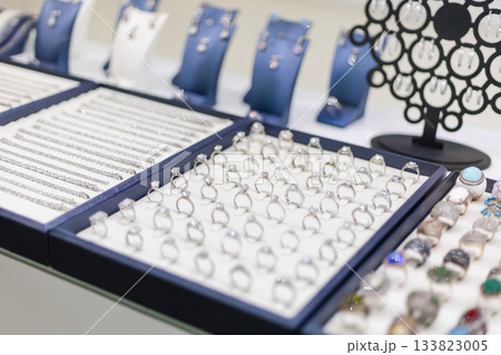 Multiple trays showcase an assortment of shiny rings and bracelets in a jewelry store. Colorful gemstones and elegant designs attract customer attention, creating a luxurious shopping experience 133823005